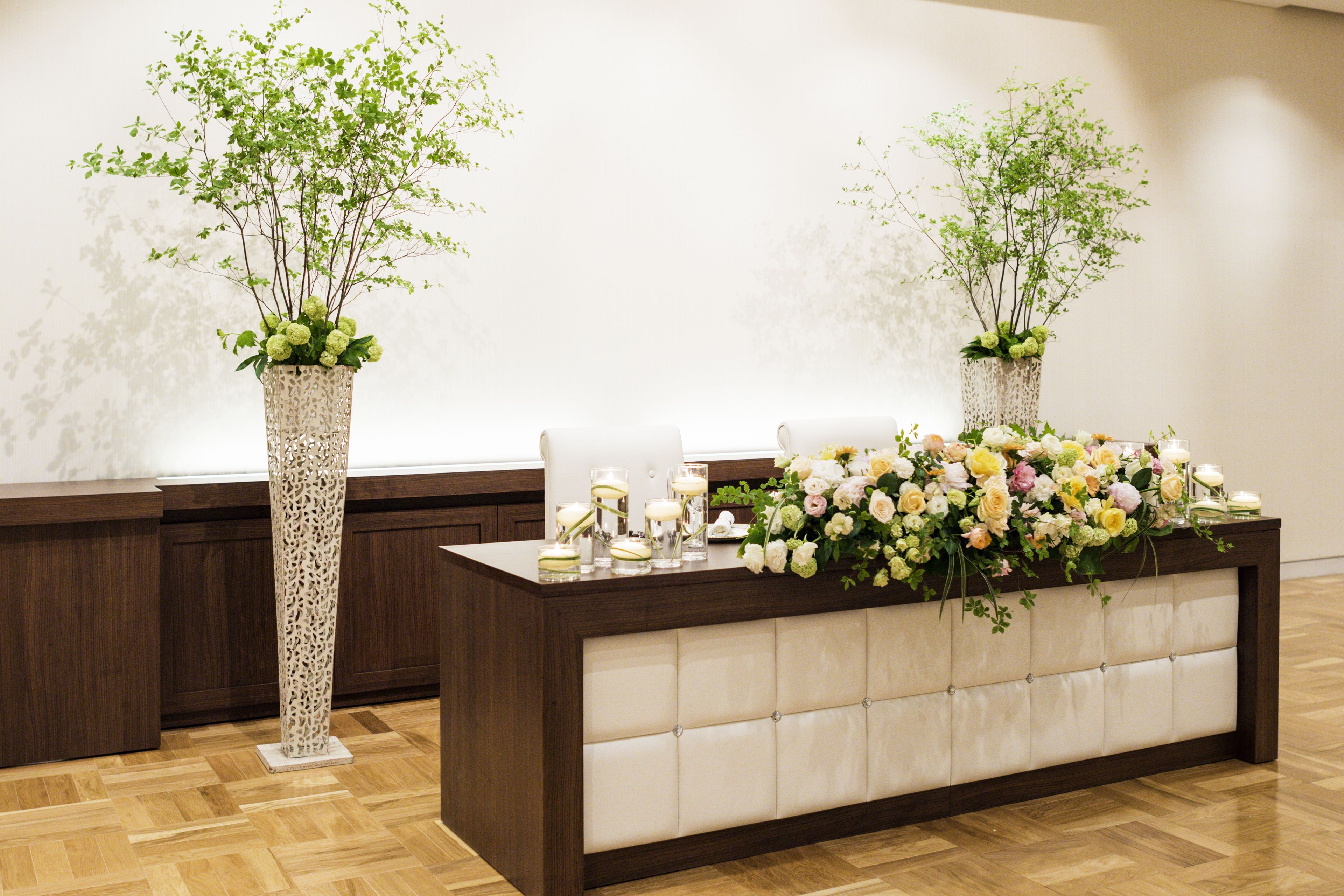 A reception desk with two tall, ornate vases, a floral arrangement, and a seating area.