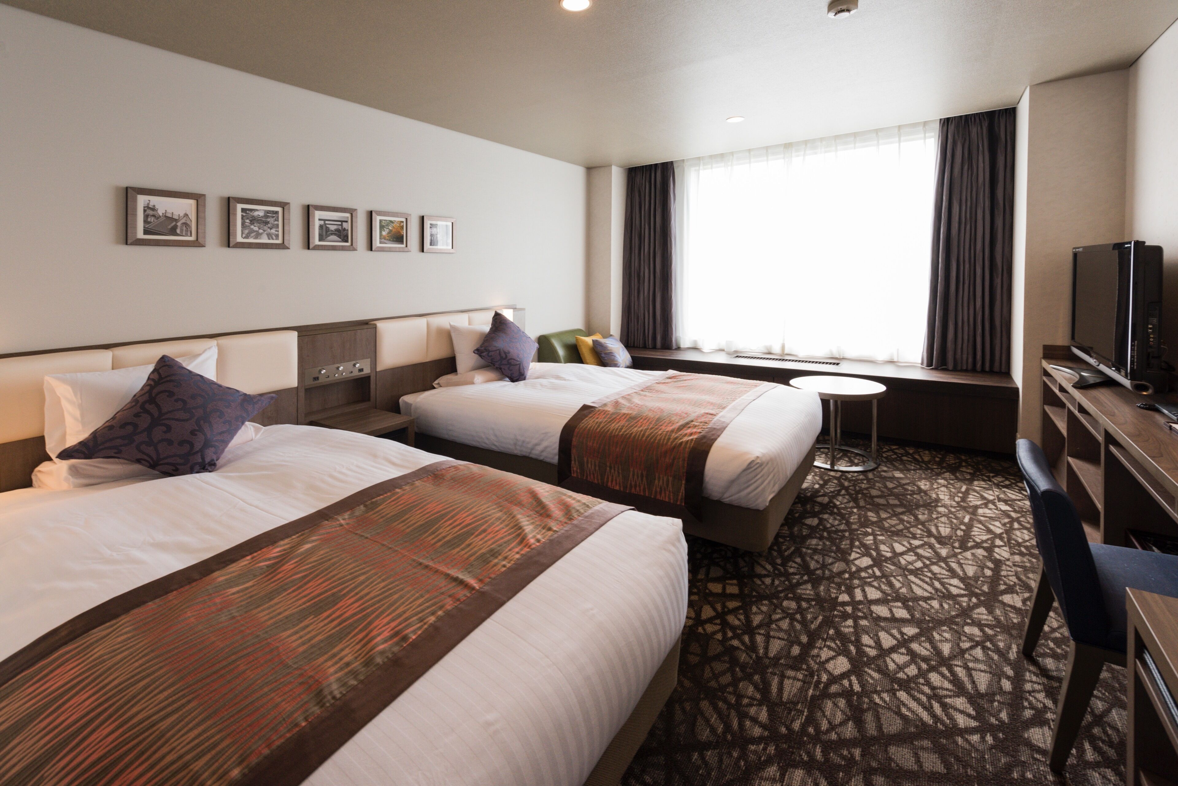 Habitación de hotel con dos camas, un escritorio, un televisor y una ventana con cortinas.