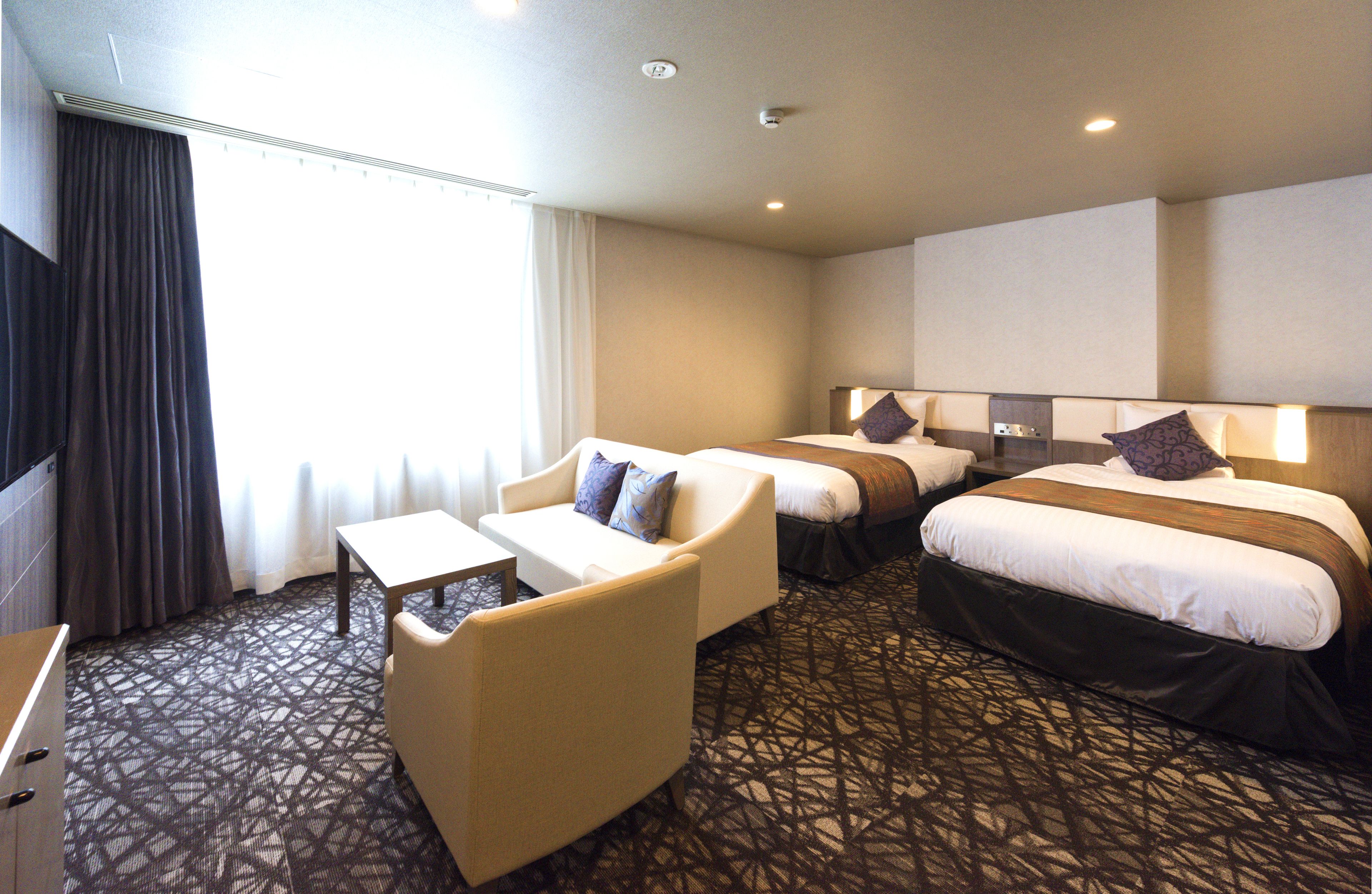 A hotel room with two beds, a sofa, a small table, and a TV.