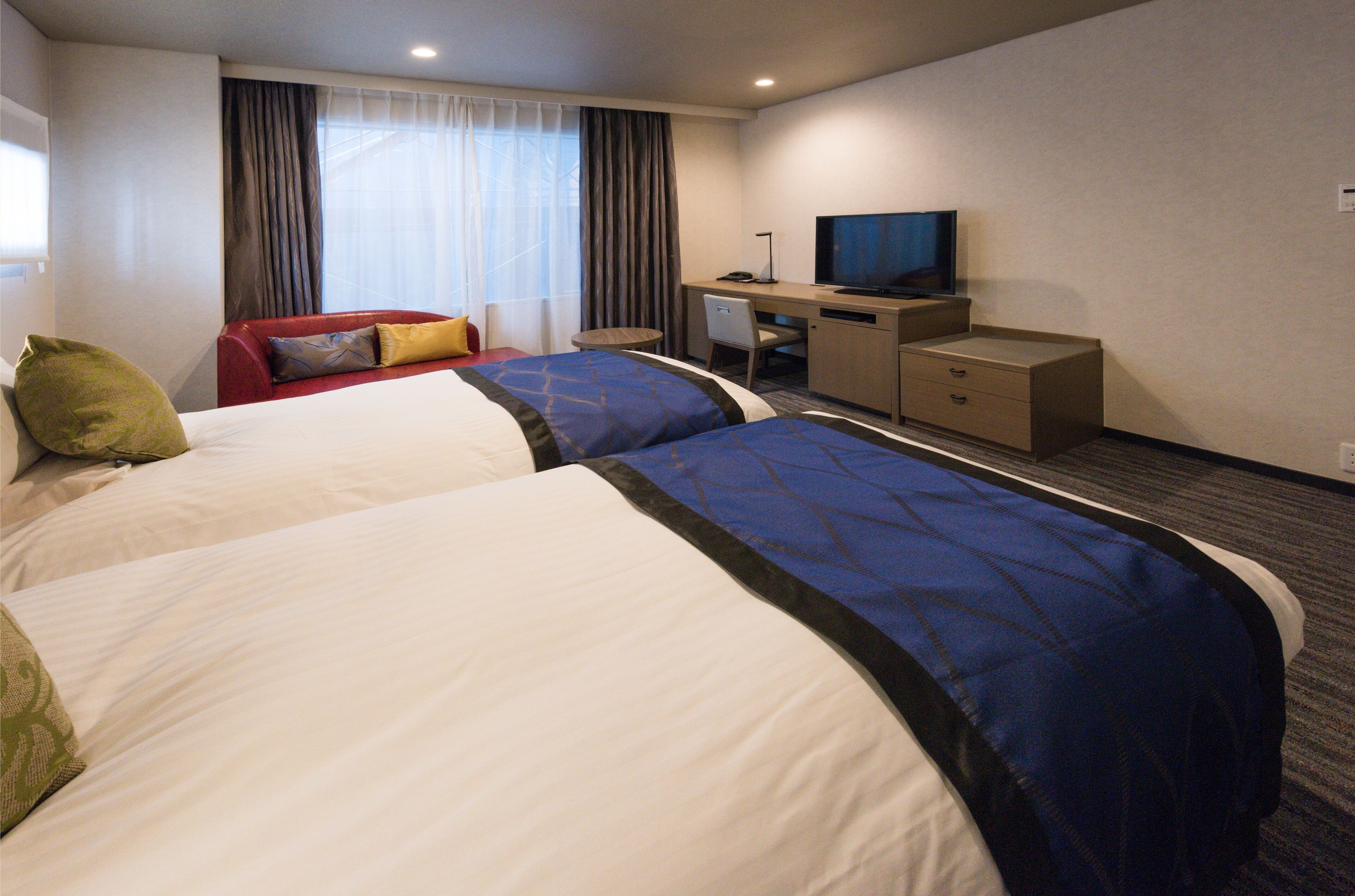 Una habitación de hotel con dos camas, un escritorio, un televisor y una ventana con cortinas.