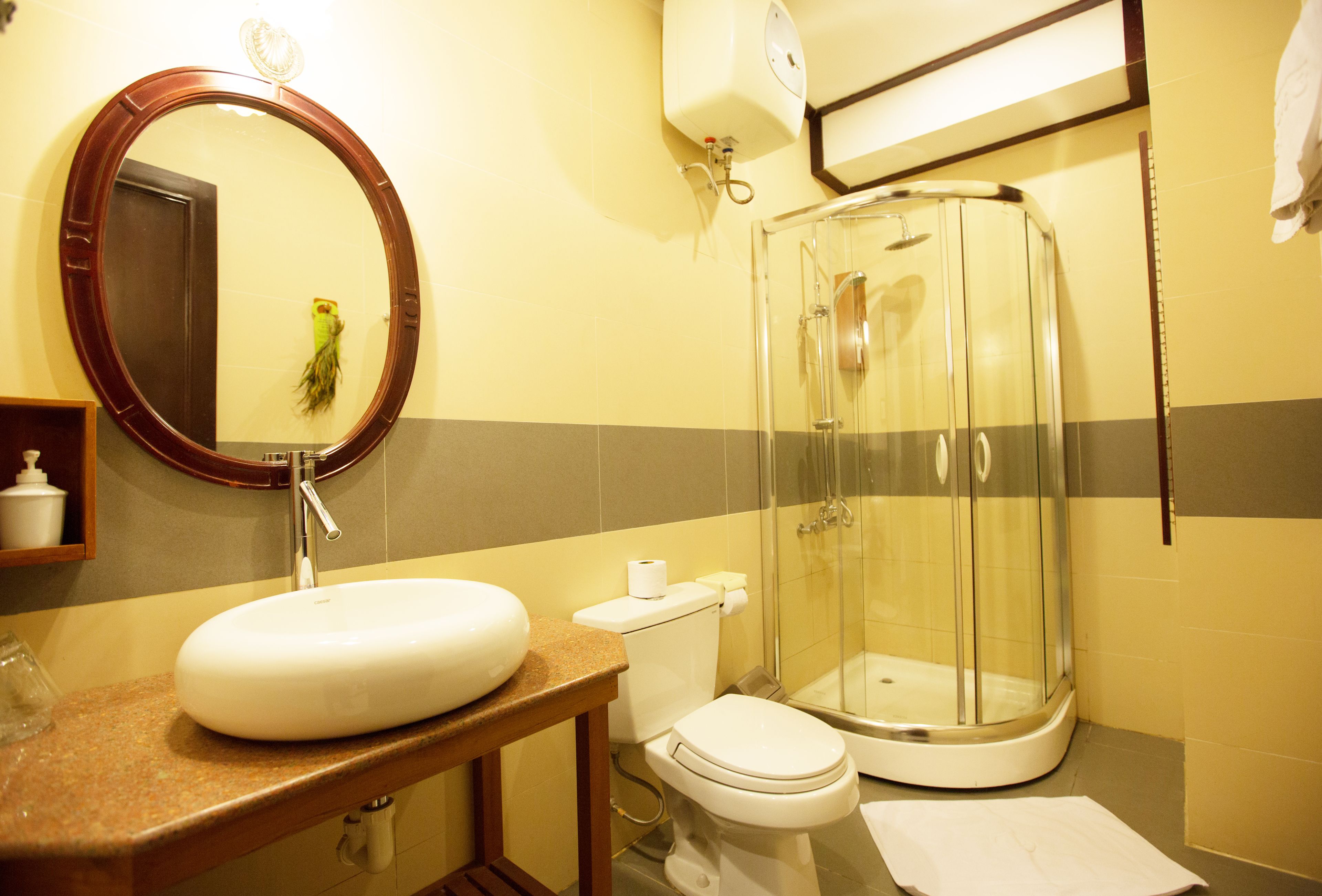 A bathroom with a round mirror, sink, toilet, and a glass-enclosed shower.
