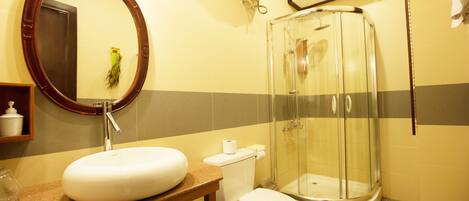 A bathroom with a round mirror, sink, toilet, and a glass-enclosed shower.