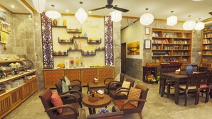 A cozy cafe with wooden furniture, a coffee bar, and a bookshelf filled with books. - Hoi An Pho Library Hotel (Da Nang)