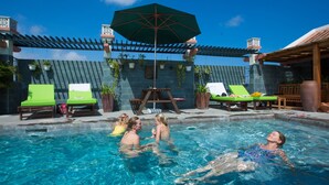A swimming pool area with lounge chairs, an umbrella, and potted plants. - Hoi An Pho Library Hotel (Da Nang)