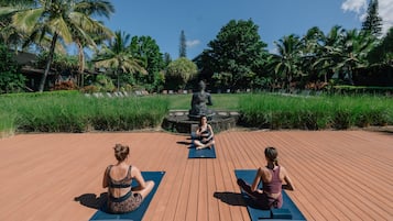 Three people sitting on yoga mats on a wooden deck with a statue in the background.