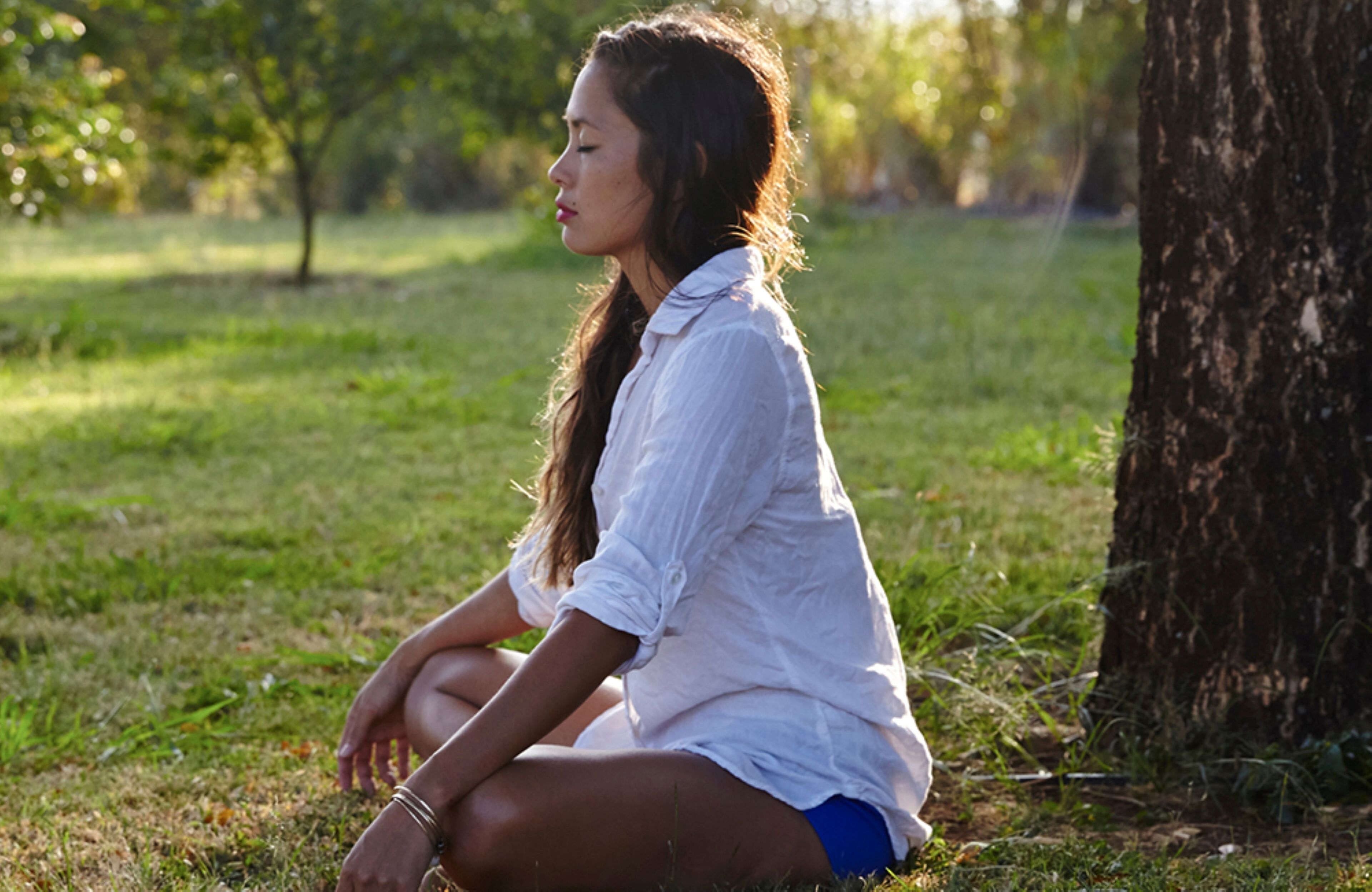 Une personne assise sur l’herbe, près d’un arbre.