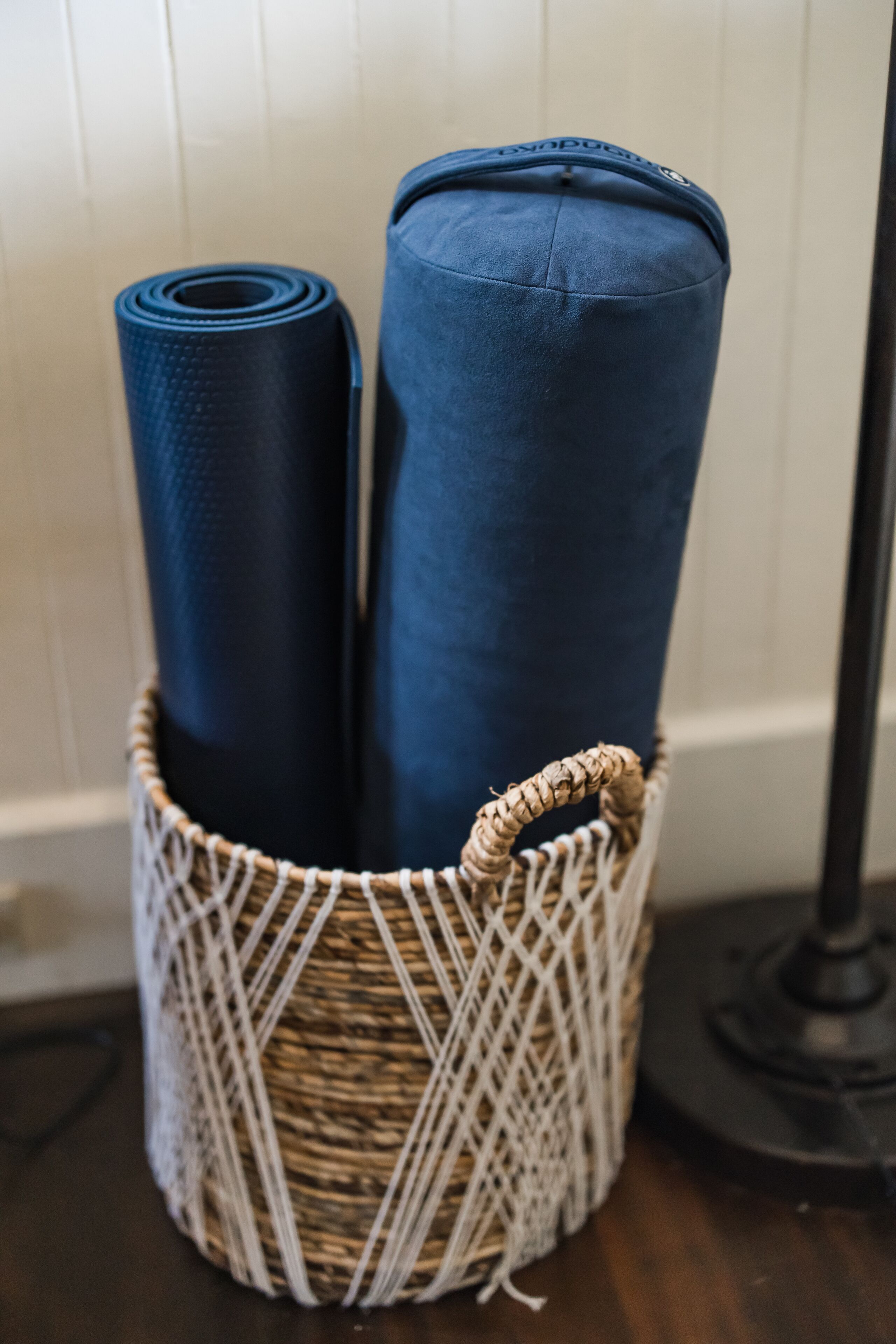A woven basket containing rolled yoga mats and a blue cushion.
