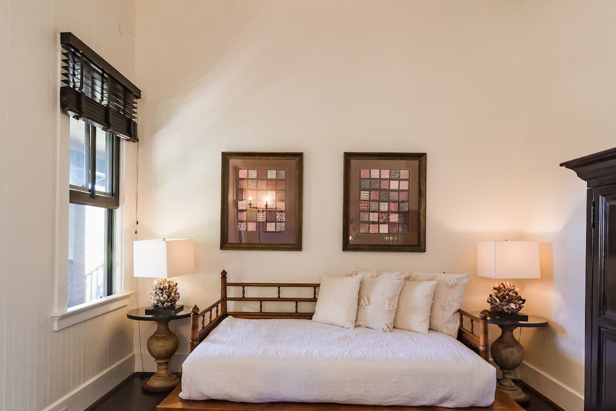 A bedroom with a bed, two wall-mounted lamps, a glass coffee table, and a window with blinds.