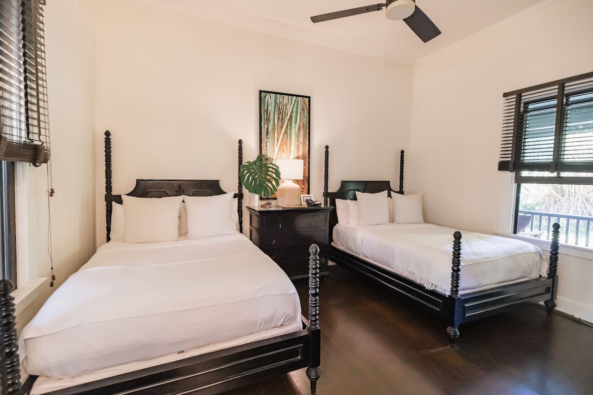 A bedroom with two beds, a nightstand, a mirror, and a window with blinds.