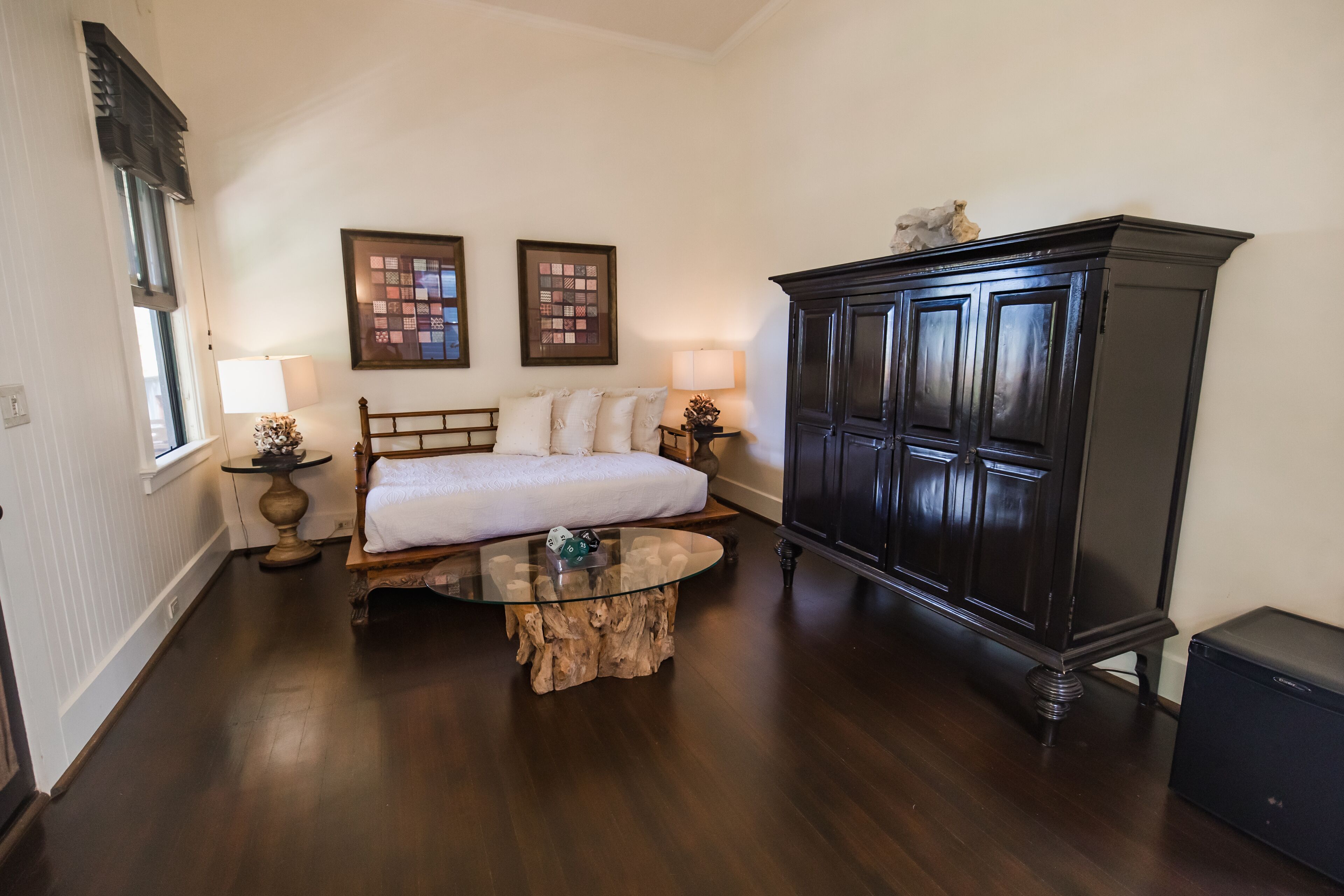 Un dormitorio con una cama, una mesa de centro redonda de vidrio, un armario de madera oscura y dos lámparas fijadas a la pared.