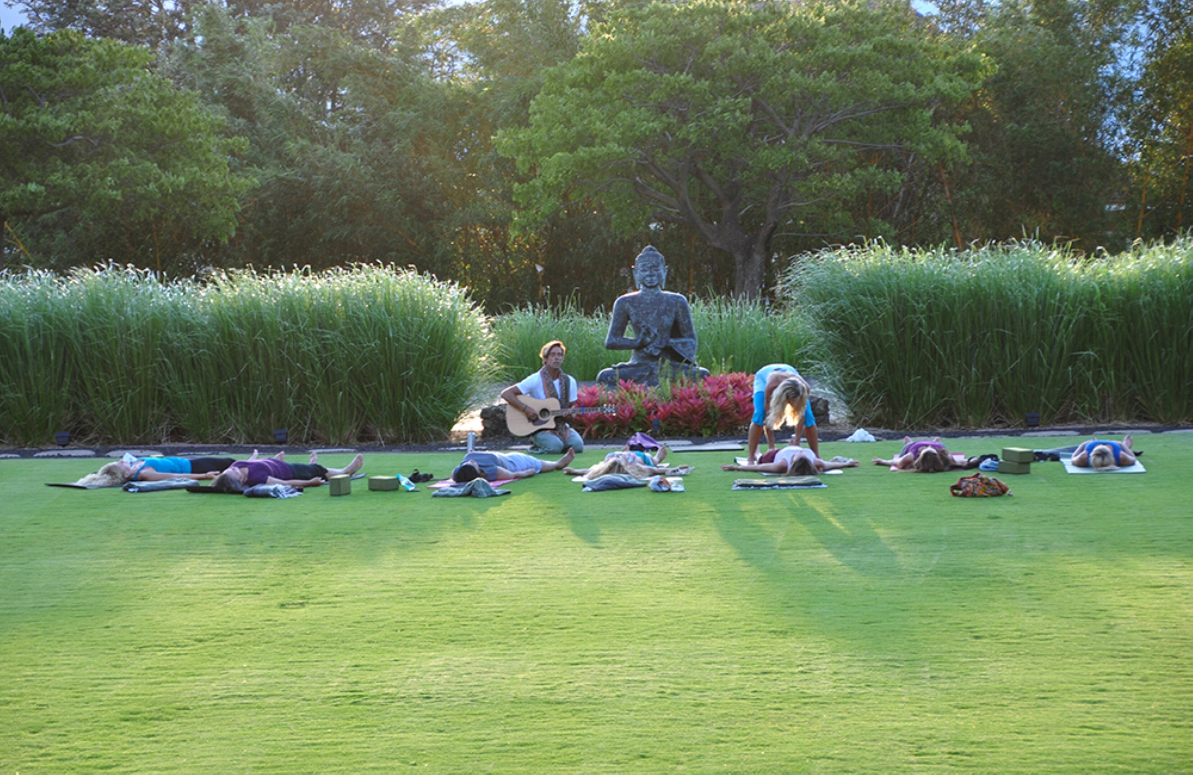 Un grupo de personas practicando yoga al aire libre en un parque, con una estatua de fondo.