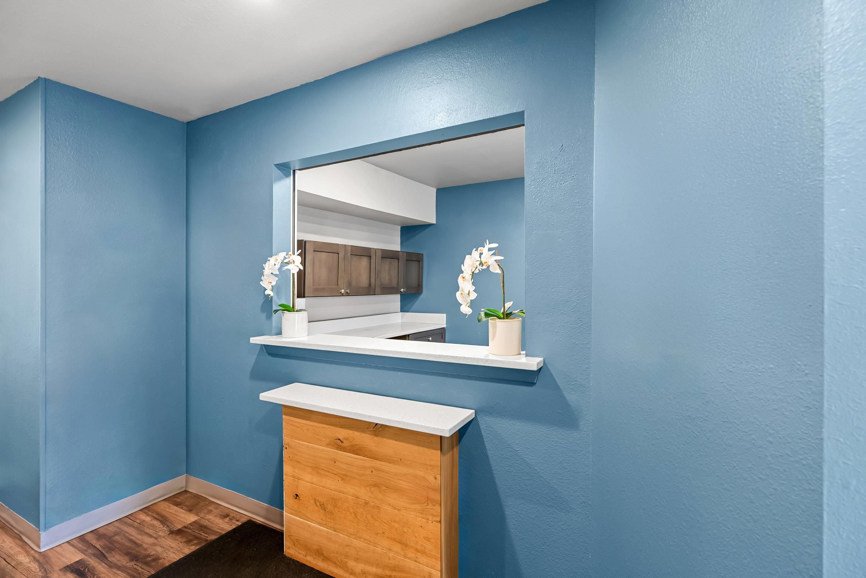 A bathroom with a blue wall, a wooden vanity, a white countertop, and two white orchids.