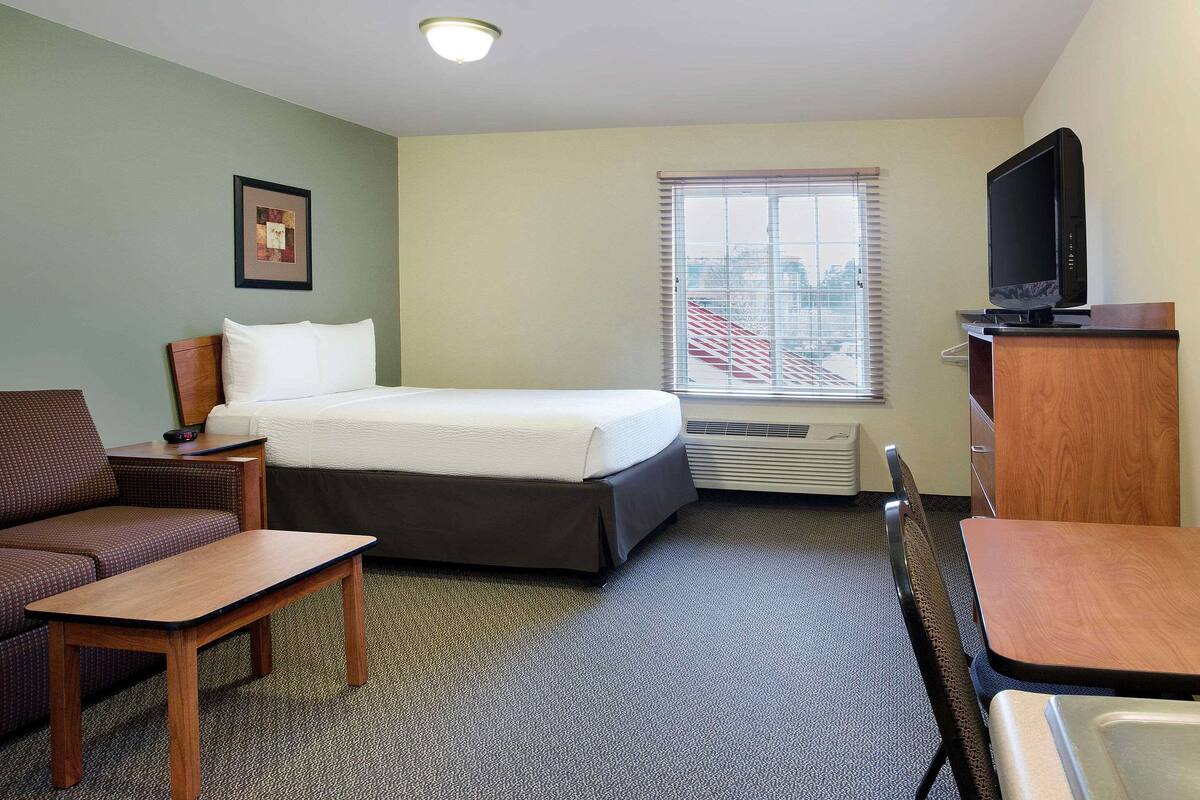 A hotel room with a bed, a desk, a chair, a television, and a window with blinds.