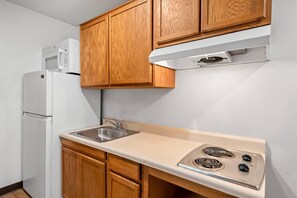 A compact kitchen with wooden cabinets, a white refrigerator, a stainless steel sink, and a built-in stove. - WoodSpring Suites Richmond West I-64 (Richmond)