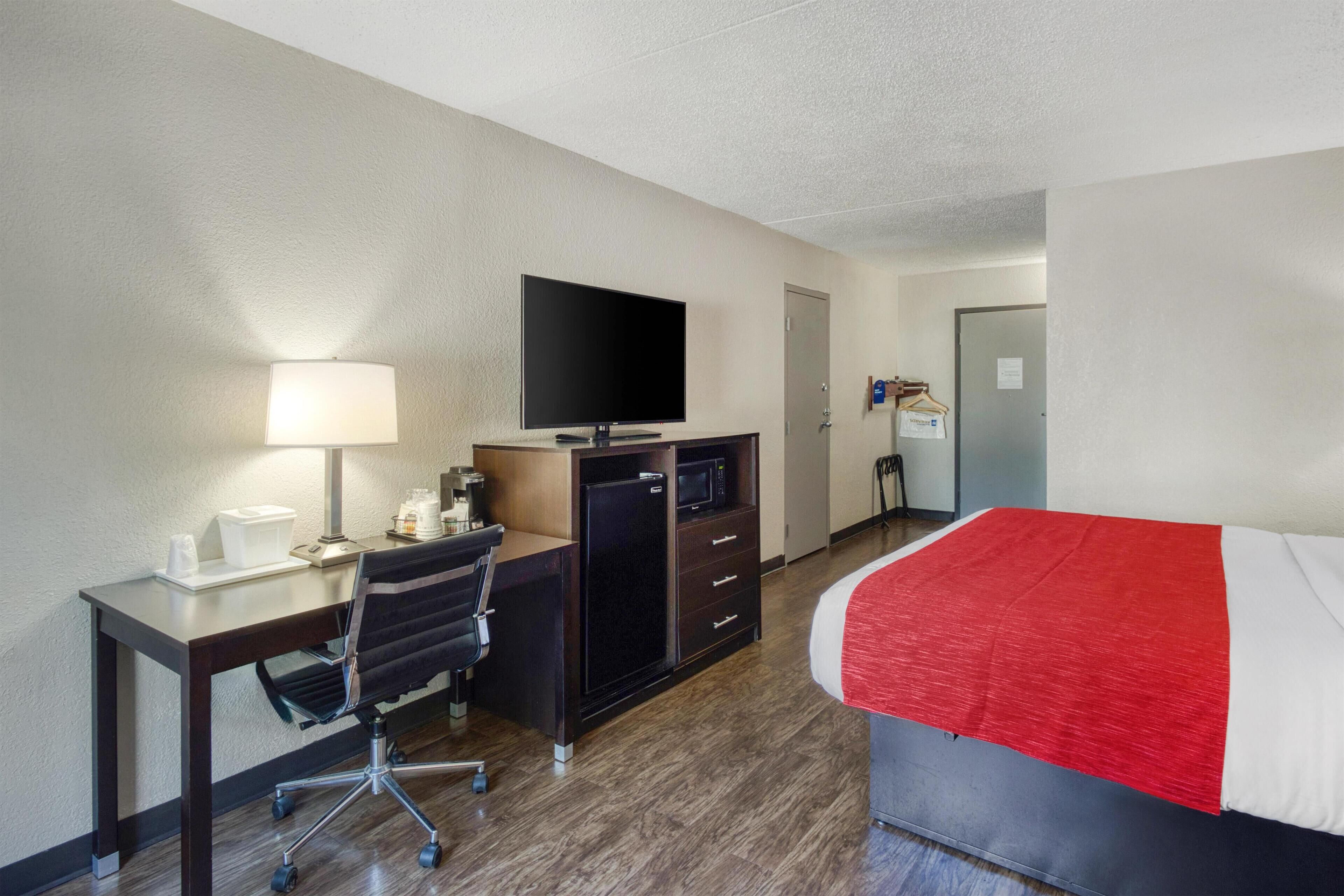 A hotel room with a bed, desk, chair, TV, and a microwave.