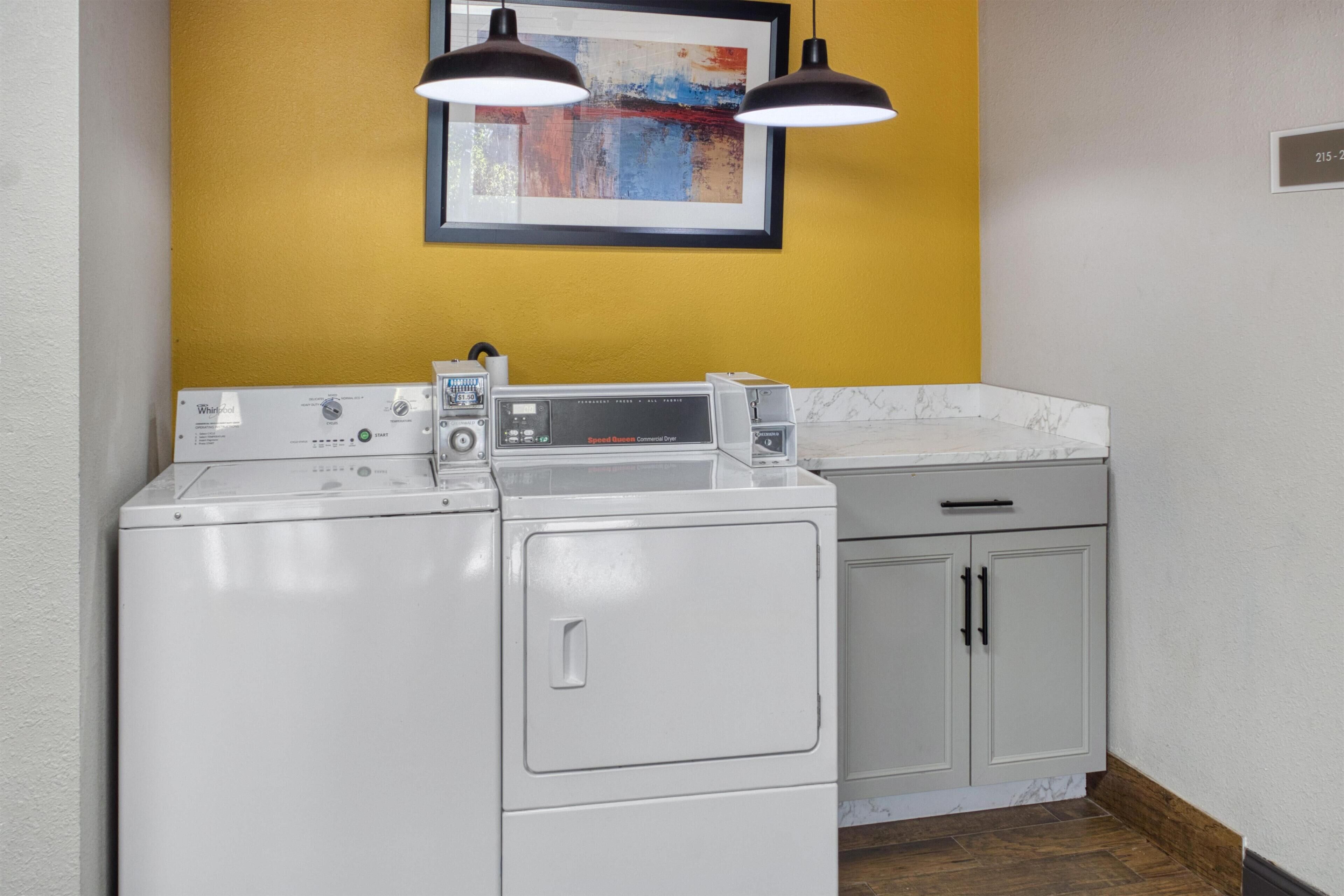 Un espace buanderie compact comprenant un lave-linge et un sèche-linge à chargement frontal, un plan de travail en marbre et un mur d’accent jaune.