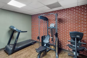 A gym with a treadmill, weight bench, and exercise equipment against a brick wall.