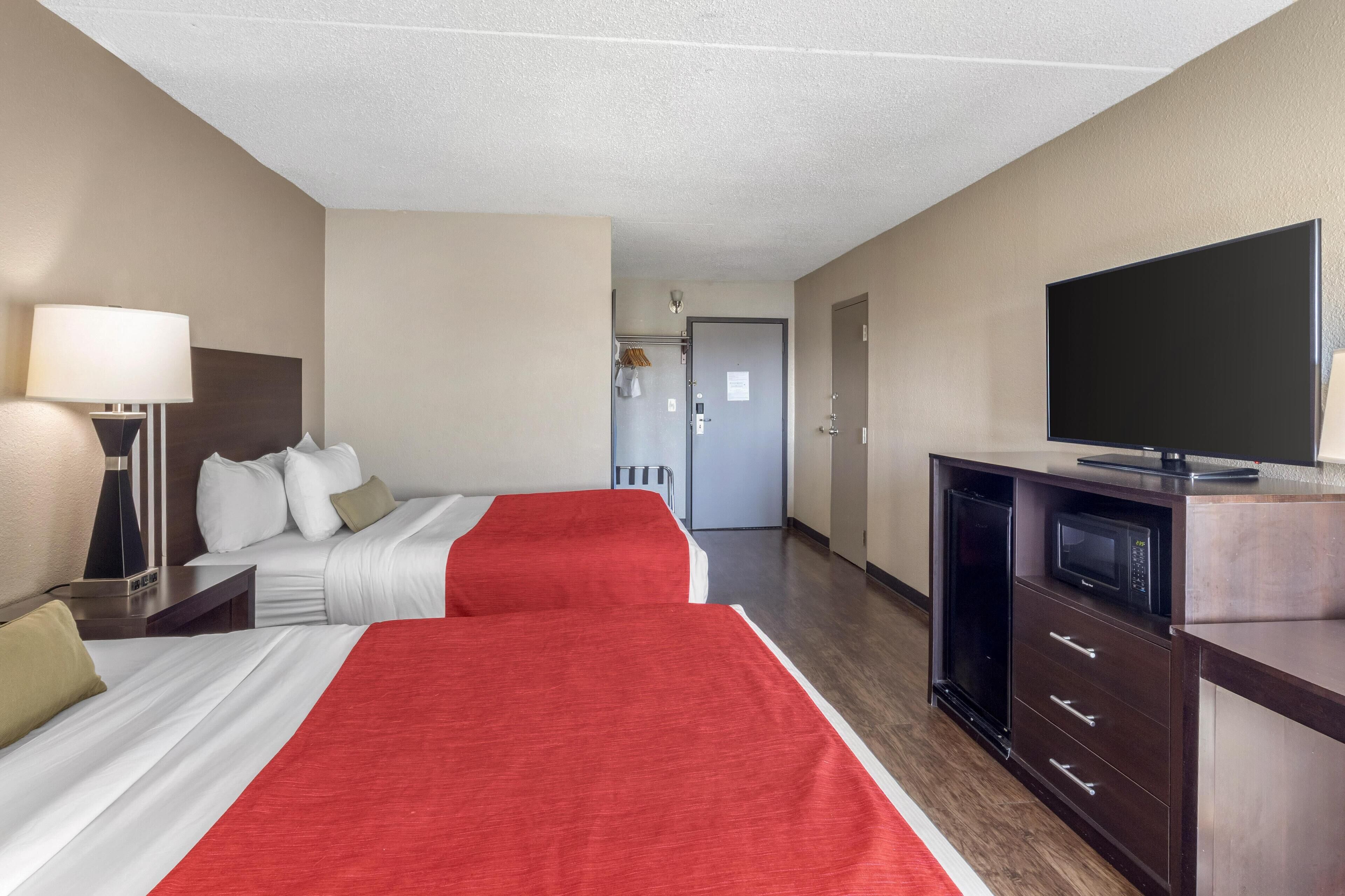 Habitación de hotel con dos camas, televisor, escritorio y microondas.