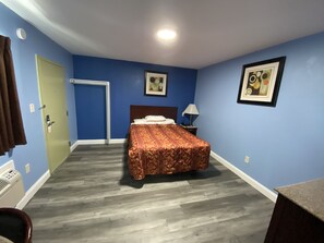Una habitación con cama, mesita de noche, lámpara y puerta.