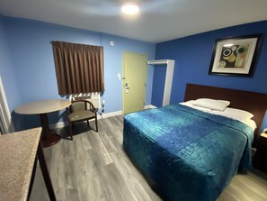 Habitación de hotel con cama, una silla, una mesita, una puerta y un equipo de aire acondicionado.