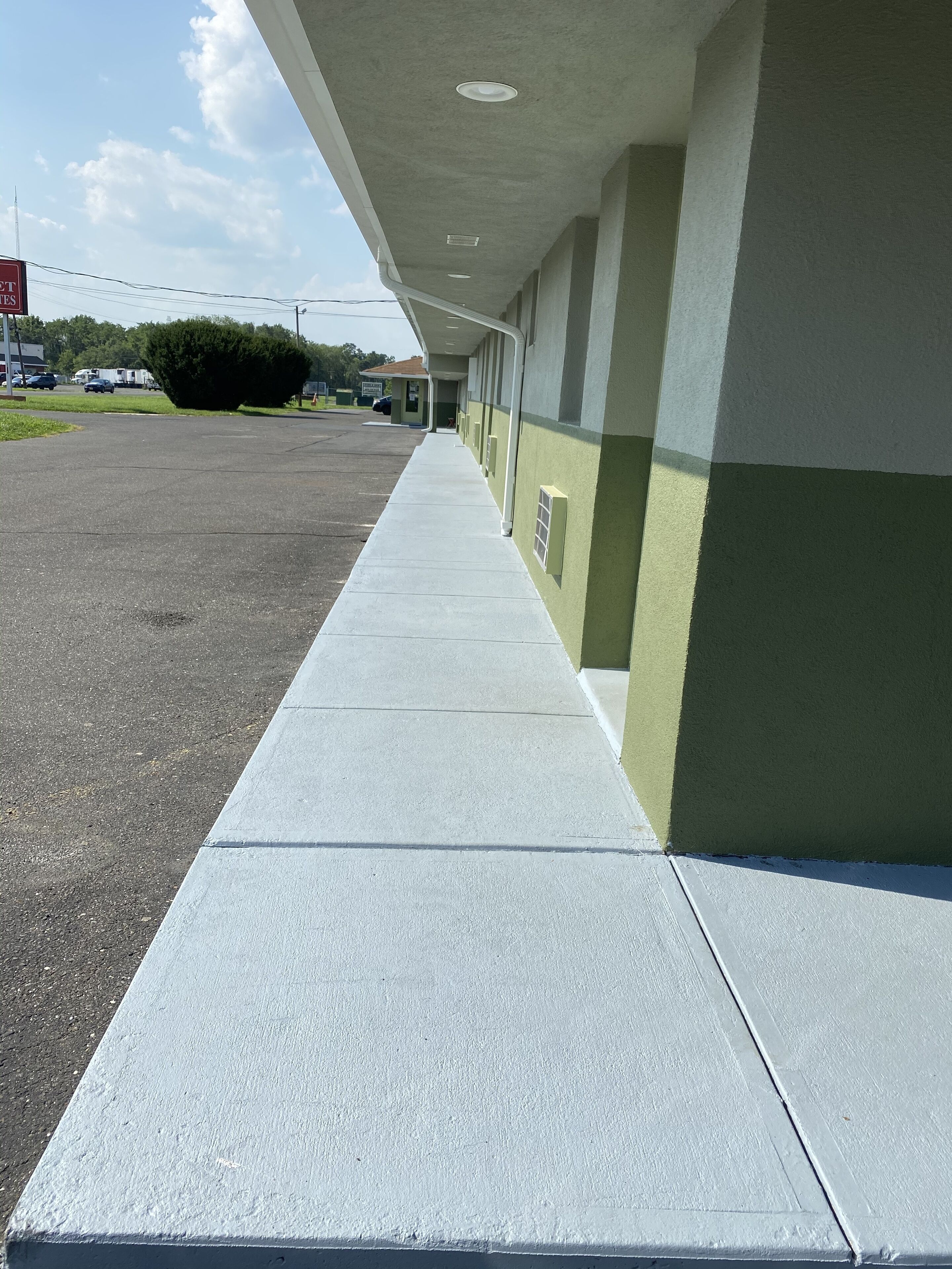 A long, straight concrete pathway leading to a building with a flat roof and a green and white exterior.