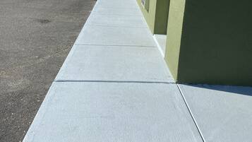 A long, straight concrete pathway leading to a building with a flat roof and a green and white exterior.