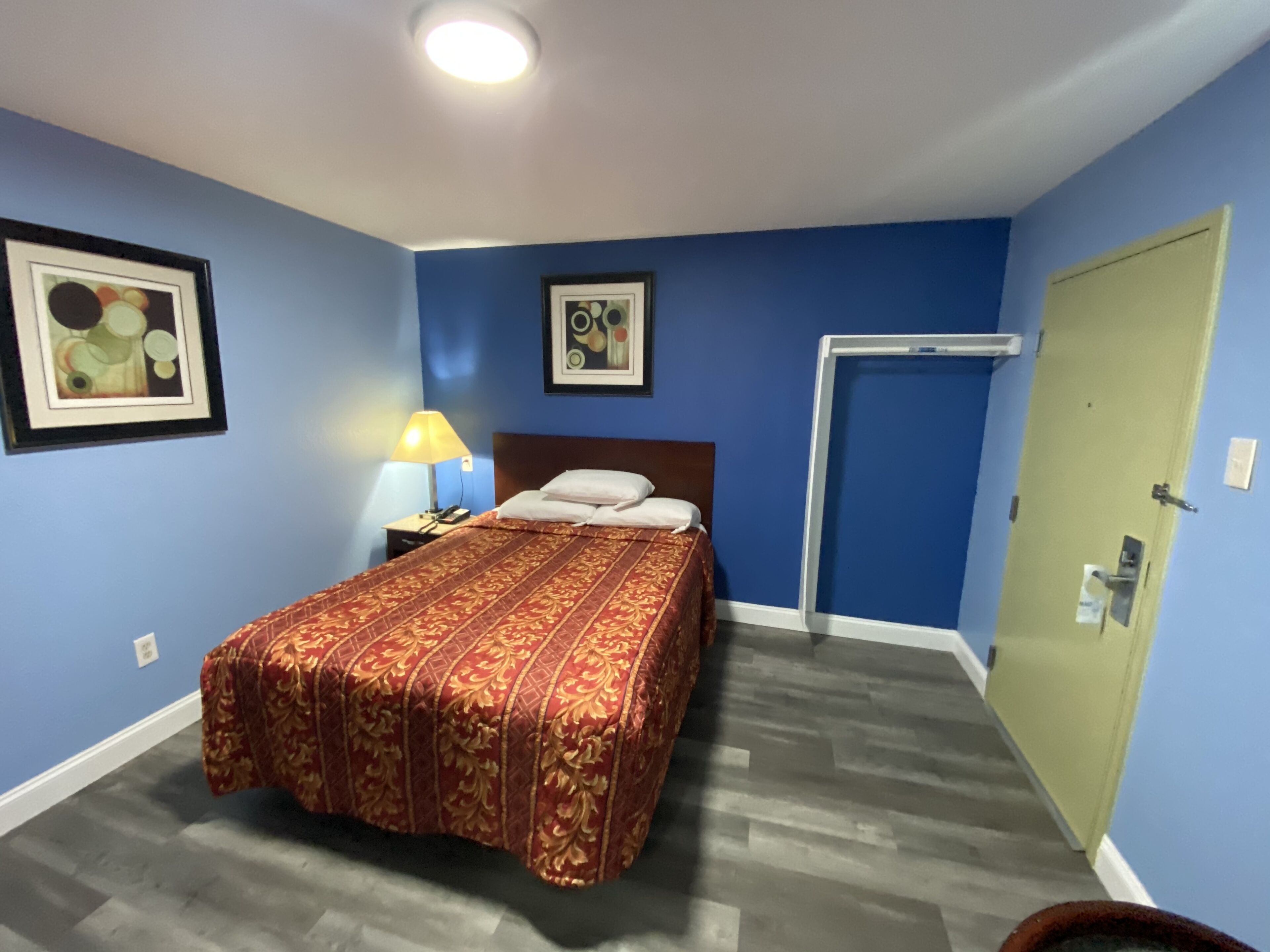 Un dormitorio con cama, mesita de noche, lámpara y dos cuadros en la pared.