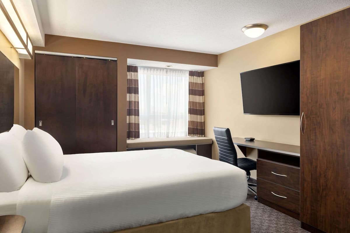 Ein Hotelzimmer mit Bett, Schreibtisch, Stuhl, Fernseher und Kleiderschrank.