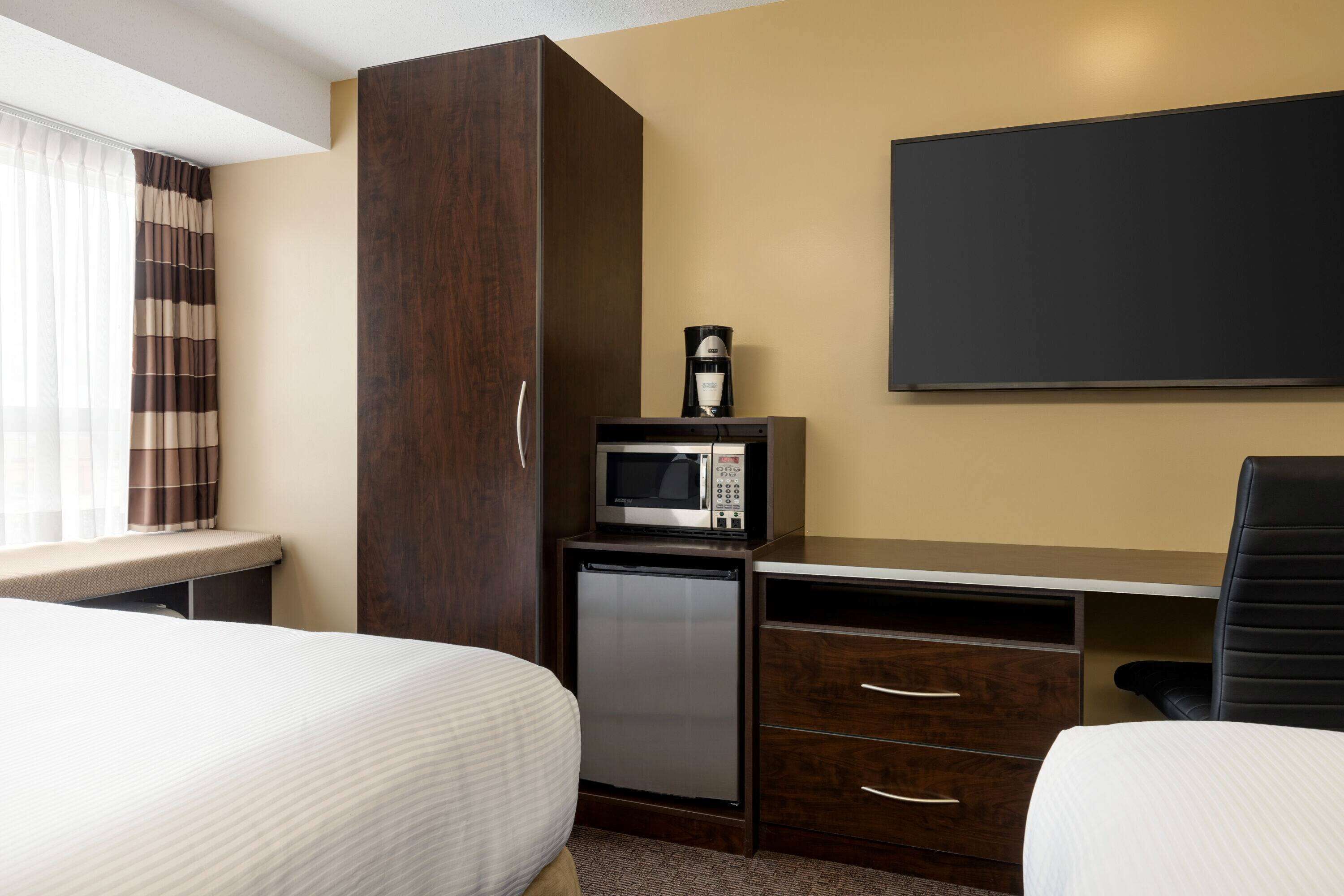 Una habitación de hotel con dos camas, un escritorio con microondas, un refrigerador pequeño y un televisor montado en la pared.