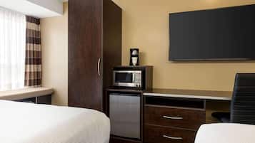 Una habitación de hotel con dos camas, un escritorio con microondas, un refrigerador pequeño y un televisor montado en la pared.