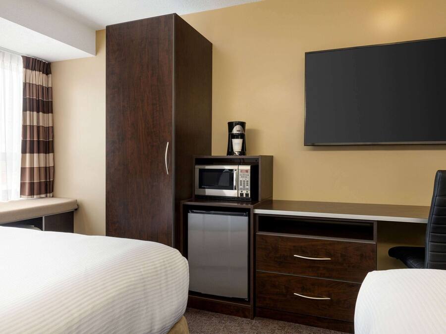Una habitación de hotel con dos camas, un escritorio con microondas, un refrigerador pequeño y un televisor montado en la pared.