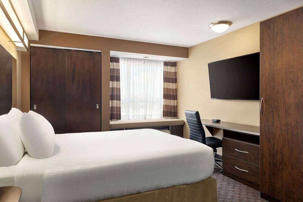 Ein Hotelzimmer mit Bett, Schreibtisch, Stuhl, Fernseher und einem Fenster mit Vorhängen.