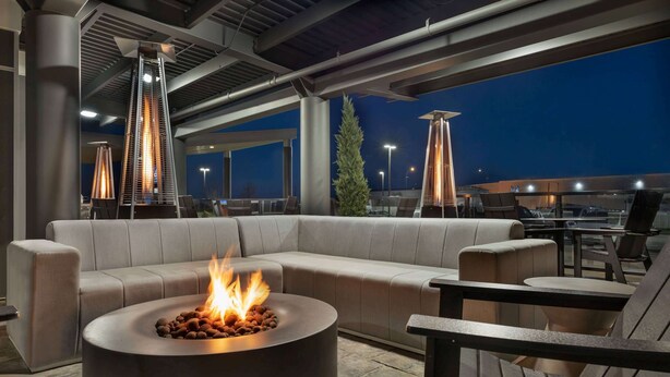 Un espacio moderno al aire libre con una chimenea circular, asientos acolchados e iluminación ambiental.