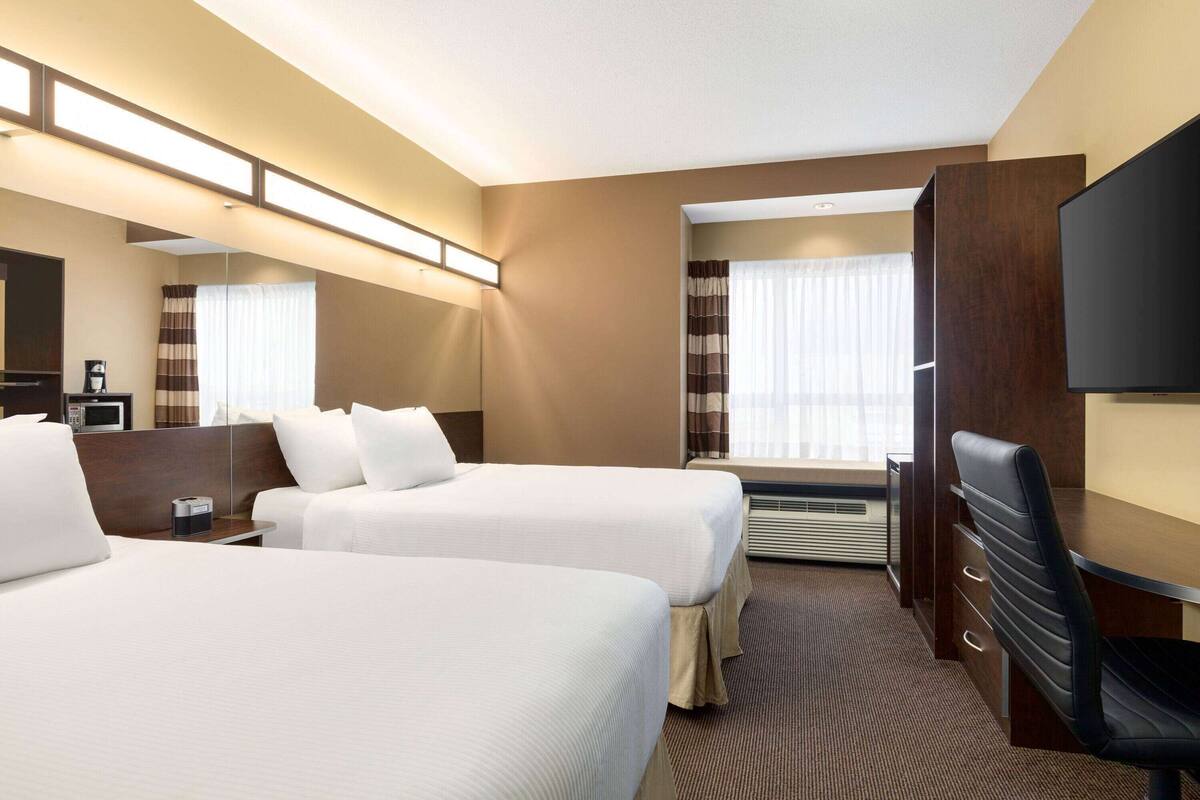 Ein Hotelzimmer mit zwei Betten, einem Schreibtisch, einem Sessel, einem Fernseher und einem großen Spiegel.