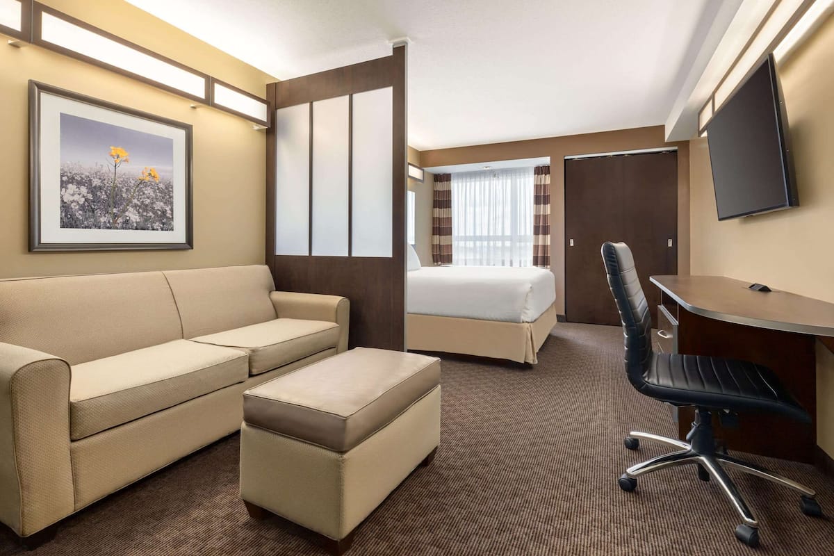 Ein Hotelzimmer mit einem Bett, einem Sofa, einem Schreibtisch, einem Stuhl, einem Fernseher und einem gerahmten Bild an der Wand.