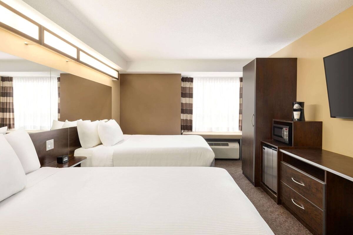 Ein Hotelzimmer mit zwei Betten, einem Fernseher, einer Mikrowelle und einem kleinen Schreibtisch.