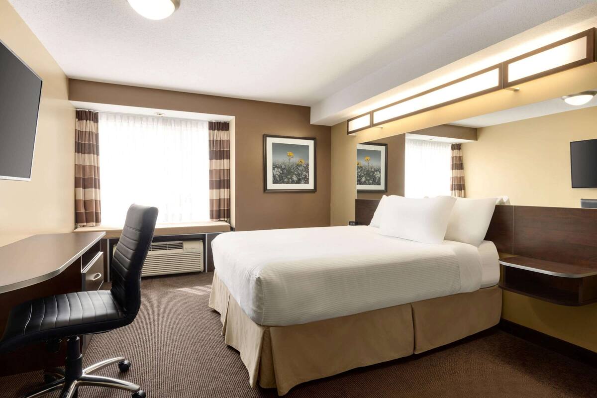 Ein Hotelzimmer mit Bett, Schreibtisch, Stuhl und großen Fenstern.