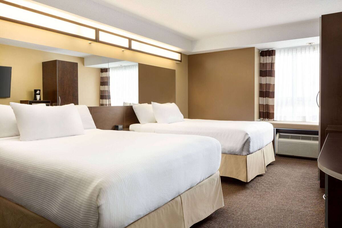 Ein Hotelzimmer mit zwei Betten, einem Flachbildfernseher, einer Minibar und einem großen Fenster mit Vorhängen.