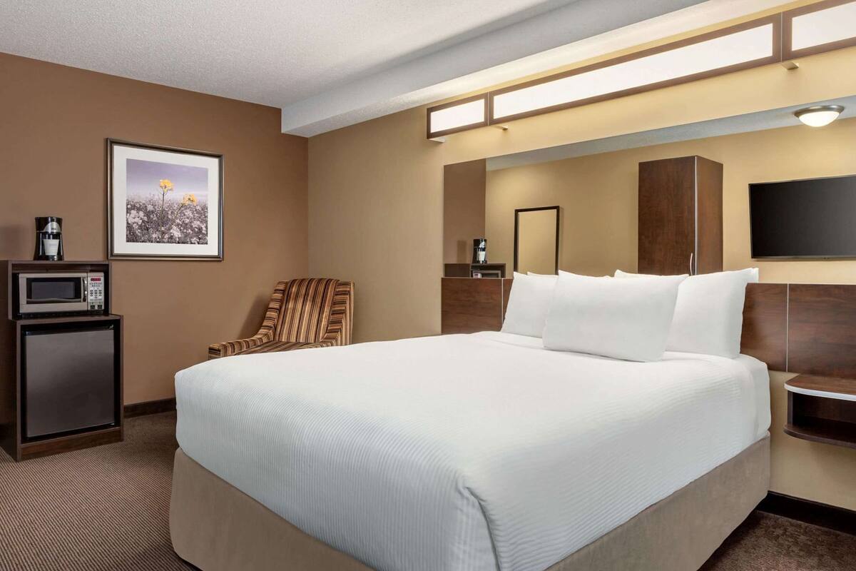Ein Hotelzimmer mit einem großen Bett, einem Sessel, einer Mikrowelle, einer Kaffeemaschine, einem gerahmten Bild, einem Spiegel und einem Fernseher.
