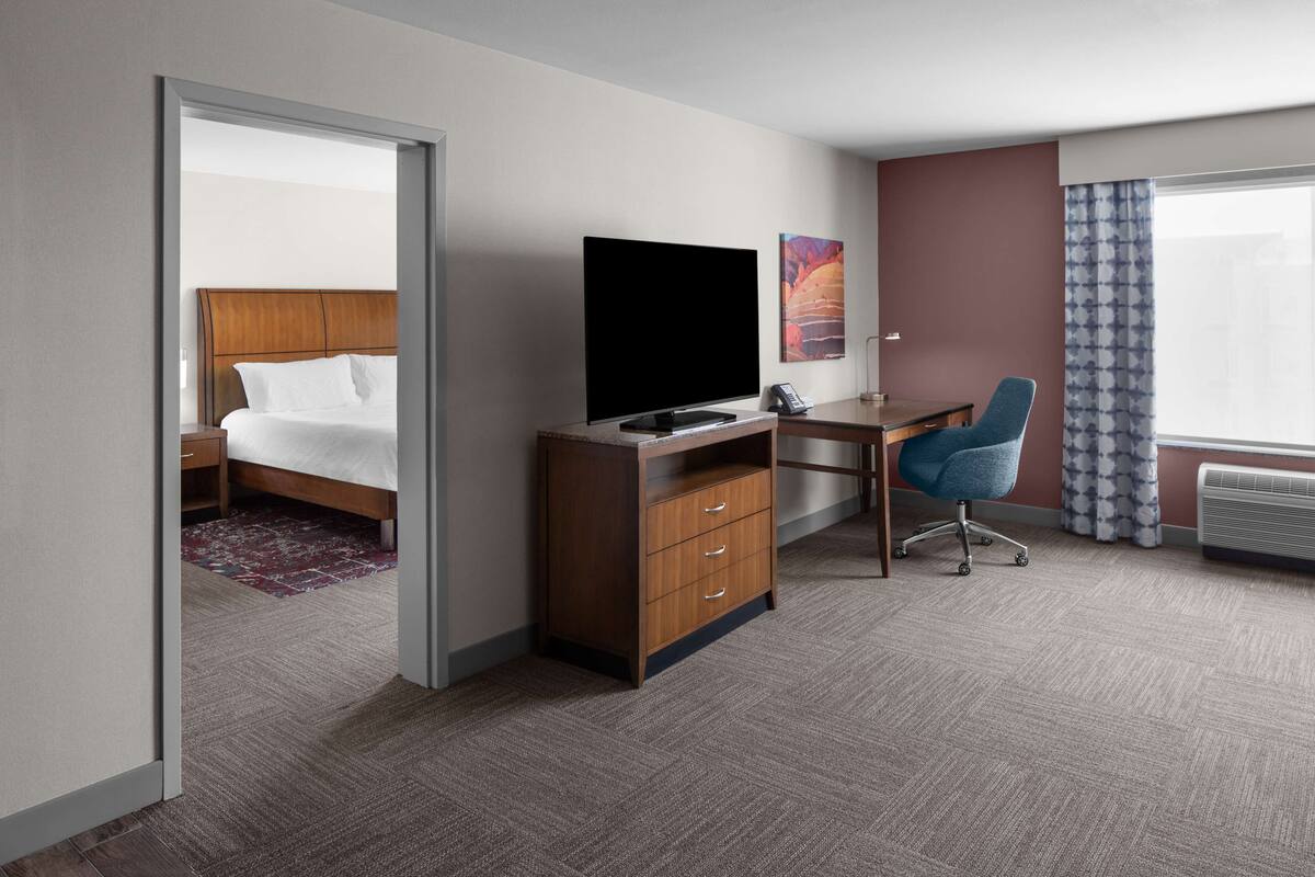 Ein Hotelzimmer mit Bett, Schreibtisch, Flachbildfernseher, Stuhl und einem fenster mit Vorhängen.
