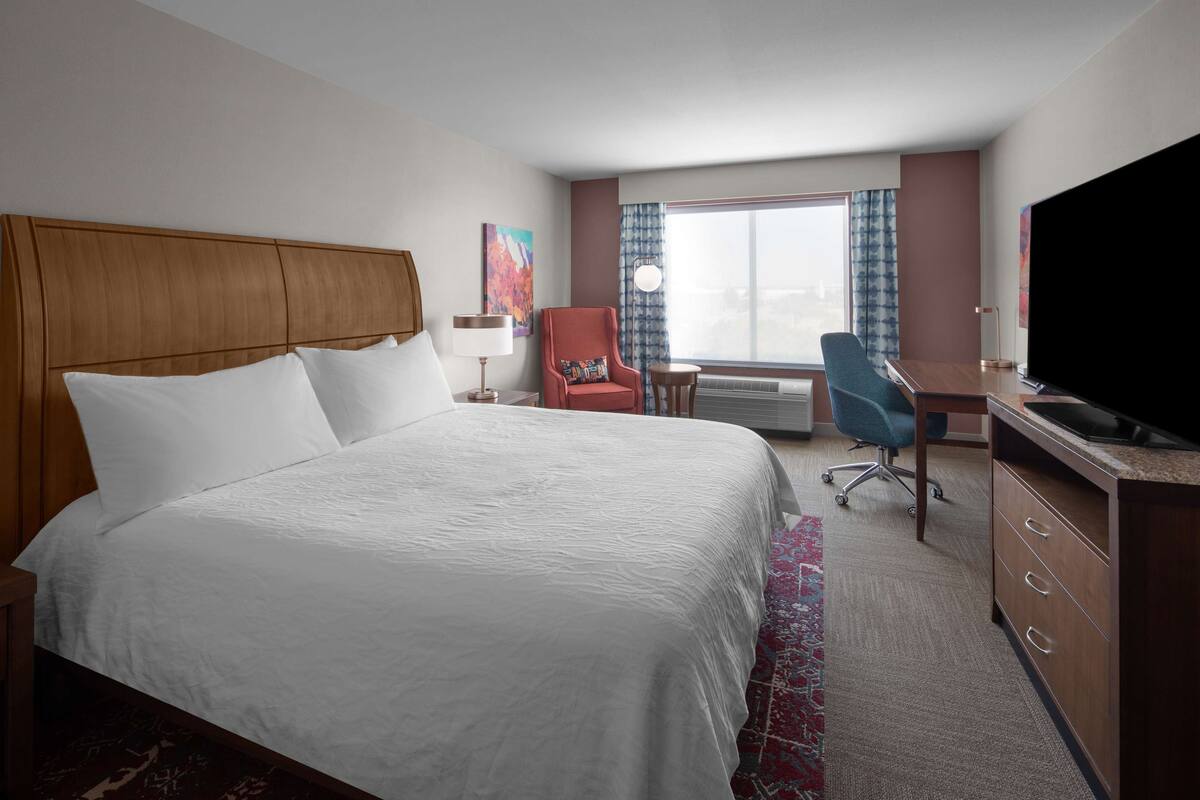 Ein Hotelzimmer mit einem großen Bett, einem Schreibtisch, einem Fernseher und einem Sessel.