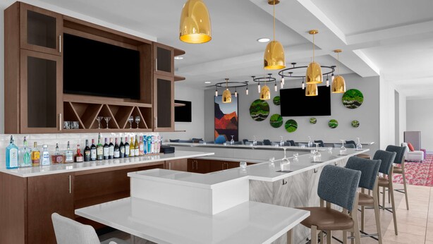 A modern bar area with a long counter, multiple seating options, and a large TV screen. - Hilton Garden Inn Salt Lake City Airport (Salt Lake City)