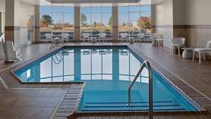 An indoor swimming pool with clear views of the outdoors, surrounded by white chairs and a tiled floor. - Hilton Garden Inn Salt Lake City Airport (Salt Lake City)