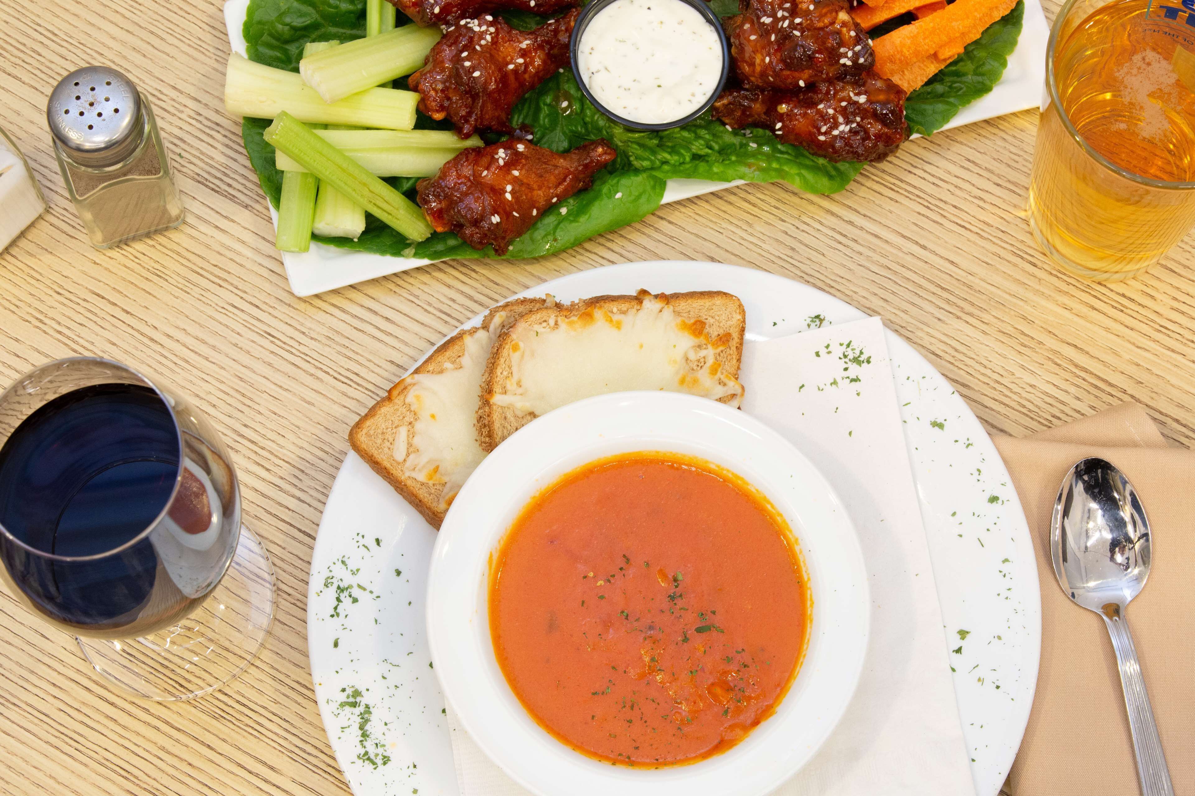 A meal consisting of a bowl of soup, a plate with two slices of bread, a side salad with chicken wings, and a glass of beer.