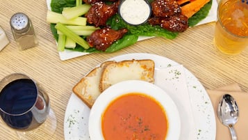 A meal consisting of a bowl of soup, a plate with two slices of bread, a side salad with chicken wings, and a glass of beer.