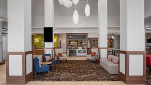 A hotel lobby with seating areas, a shop, and hanging pendant lights. - Hilton Garden Inn Salt Lake City Airport (Salt Lake City)