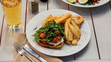 Ein Teller mit Essen, darunter ein Sandwich, Pommes und ein Salat, dazu ein Bierglas und Beilagen auf dem Tisch.
