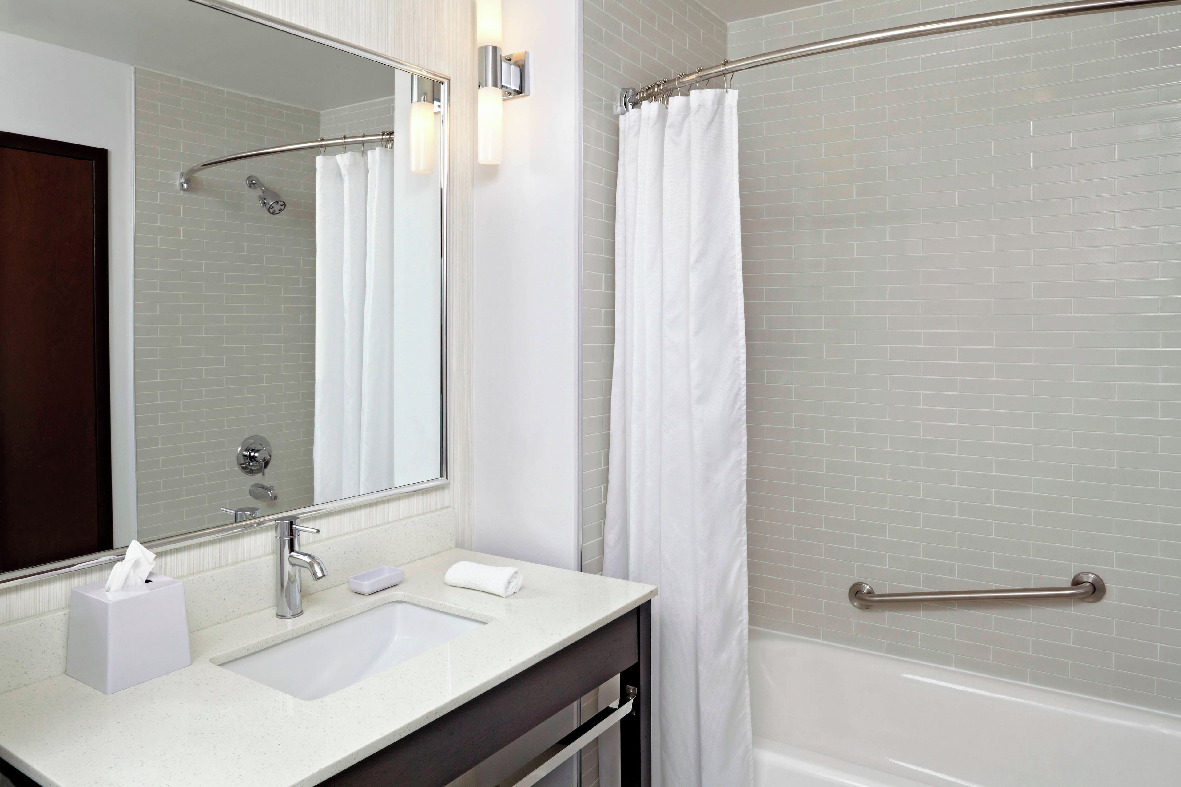A modern bathroom with a white sink, a mirror, a shower with a glass door, and a towel rack.