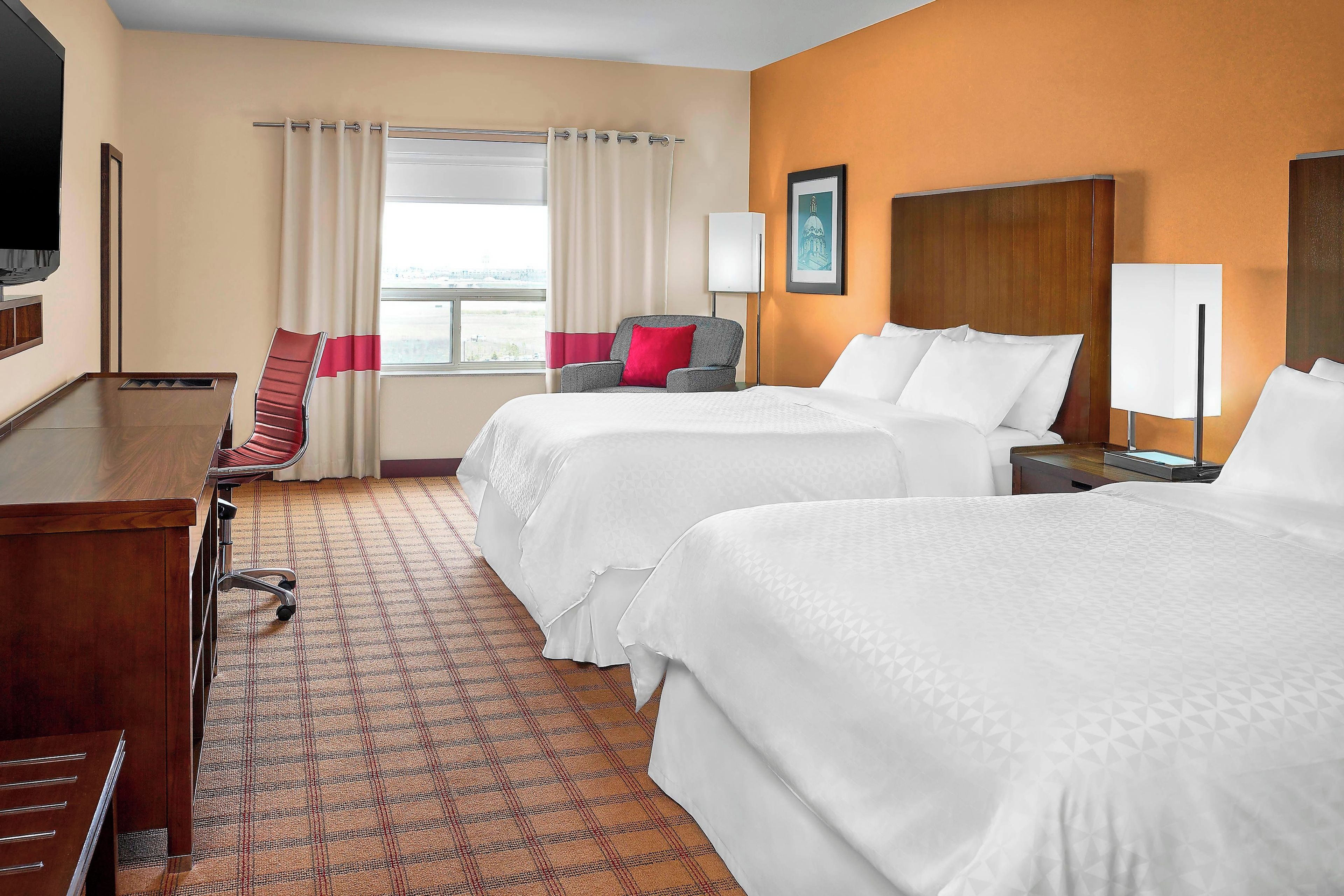 A hotel room with two beds, a desk, a chair, and a window with curtains.