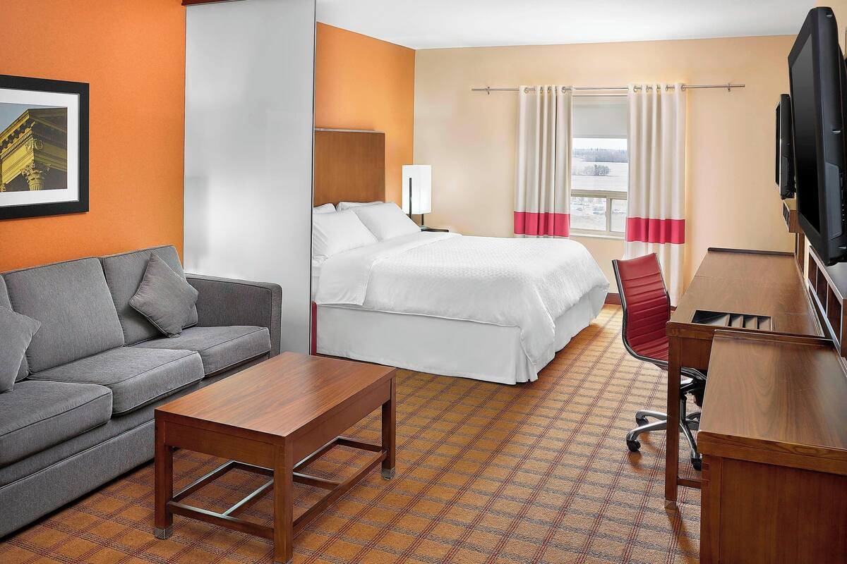 Una habitación de hotel con cama, sofá, escritorio, televisor y ventana con cortinas.